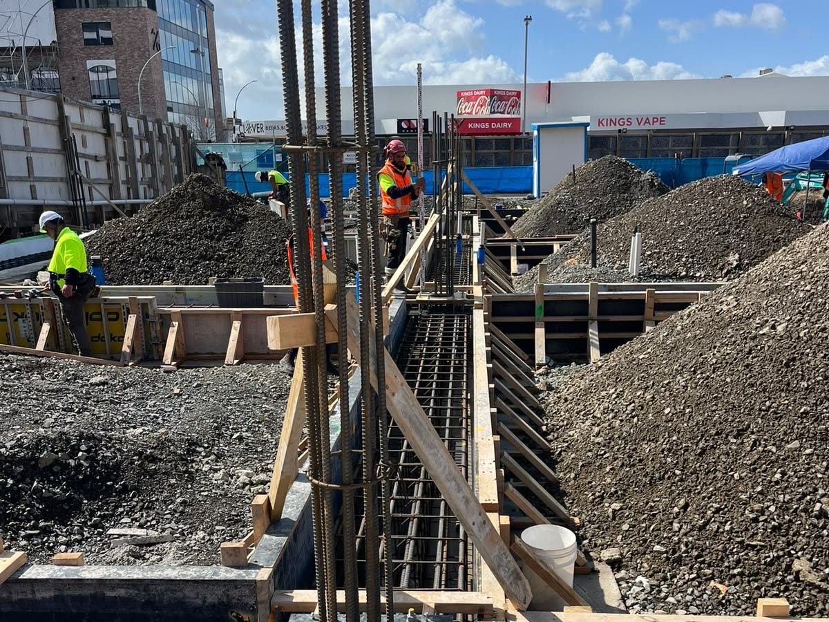 Column starter bars standing above a formed foundation beam on an urban construction site