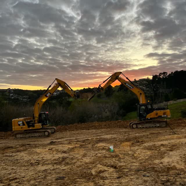 Two excavators parked on a cut building platform at sunset