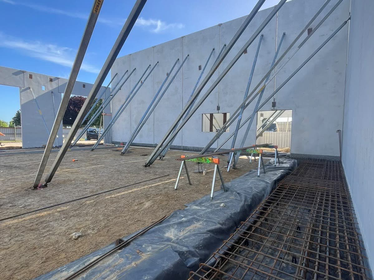 Propped precast concrete wall panels standing beside a reinforced footing on a new build