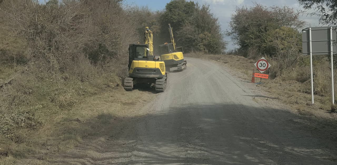 Two excavators working a metalled road shoulder past a temporary 30 kilometre speed sign
